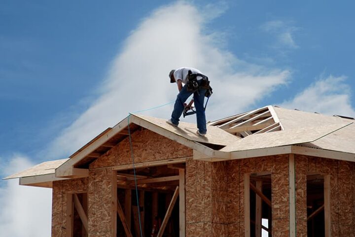 Construction worker adding roofing to frame work.