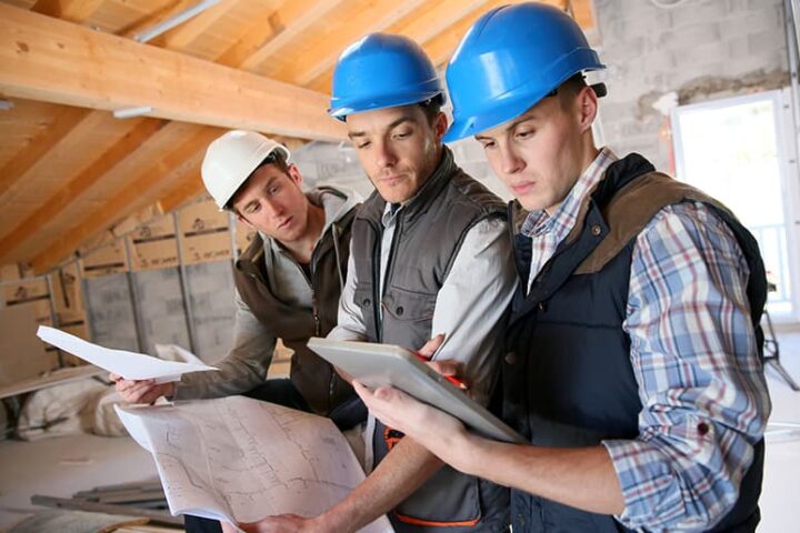 Three male construction workers looking at a blueprint and tablet