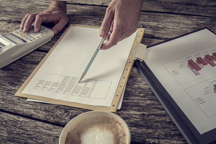 Close up of a desk with a person using a calculator and doing paperwork.