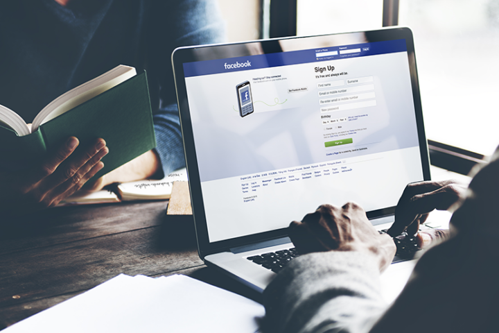 Man signing up for Facebook on his laptop while his friend reads in the background