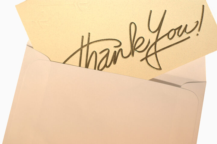 A tan card with "thank you" written in gold sticking out of a brown envelope