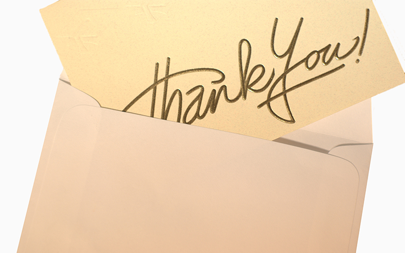 A tan card with "thank you" written in gold sticking out of a brown envelope