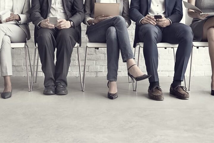 Closeup of the laps and legs of people holding various papers and mobile phones seated in a row