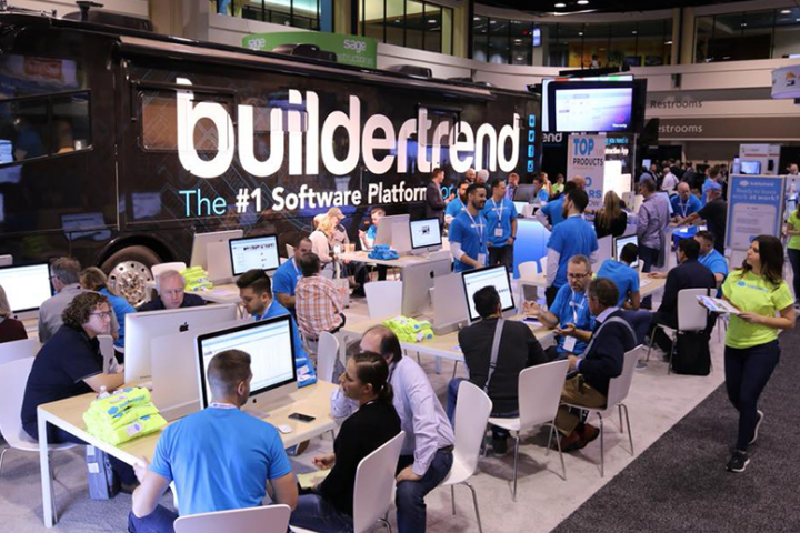 A crowd of people talking and seated at several desks with computers