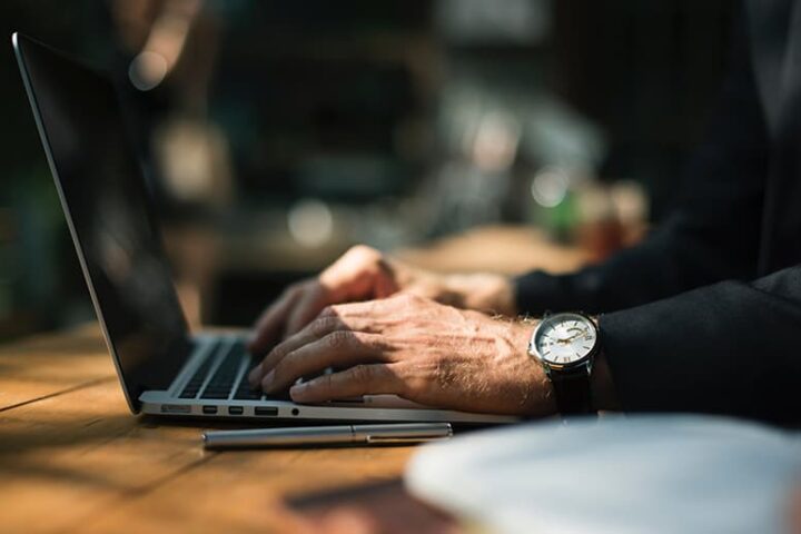 Hands with a wristwatch typing on a laptop