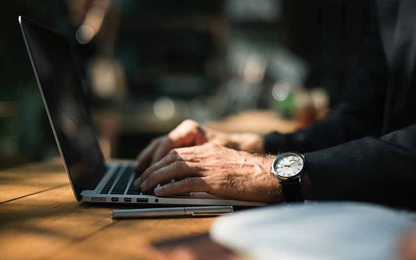 Hands with a wristwatch typing on a laptop