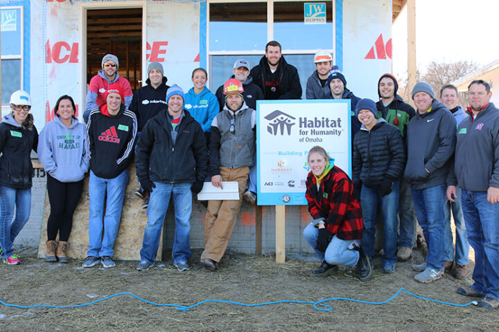 A group of Buildertrend employees posing in front of an under construction house with "Habitat for Humanity of Omaha" sign