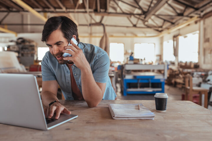Person in a work shop using a laptop and speaking on the phone