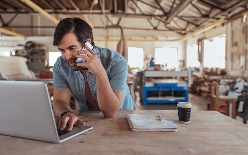 Person in a work shop using a laptop and speaking on the phone