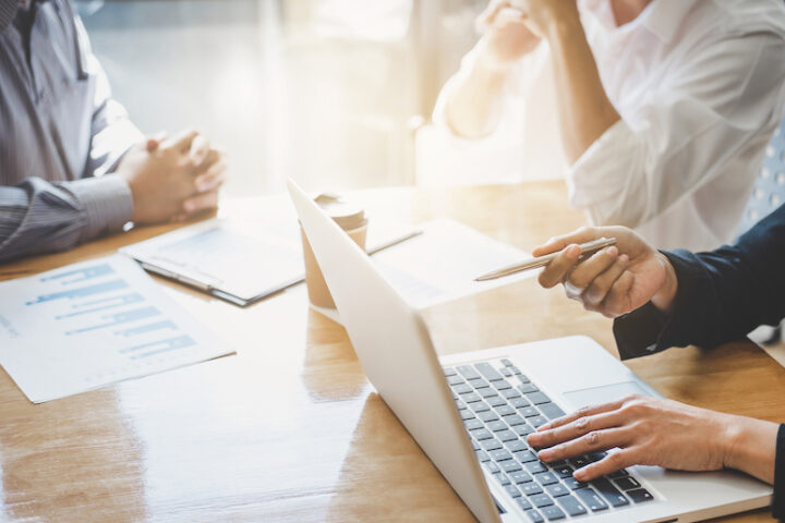 Three people at a desk with papers and a laptop