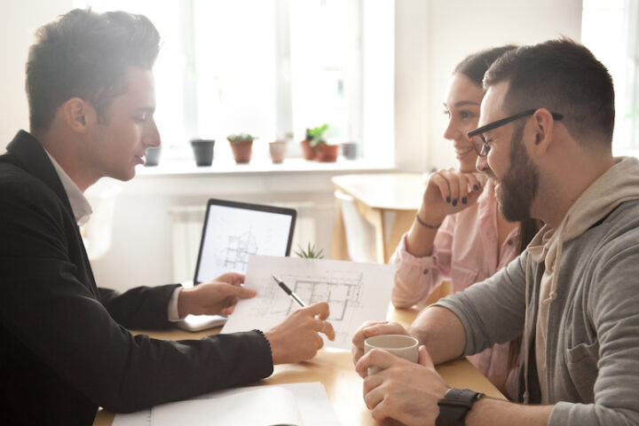 A couple seated at a desk across from a person showing them a floor plan