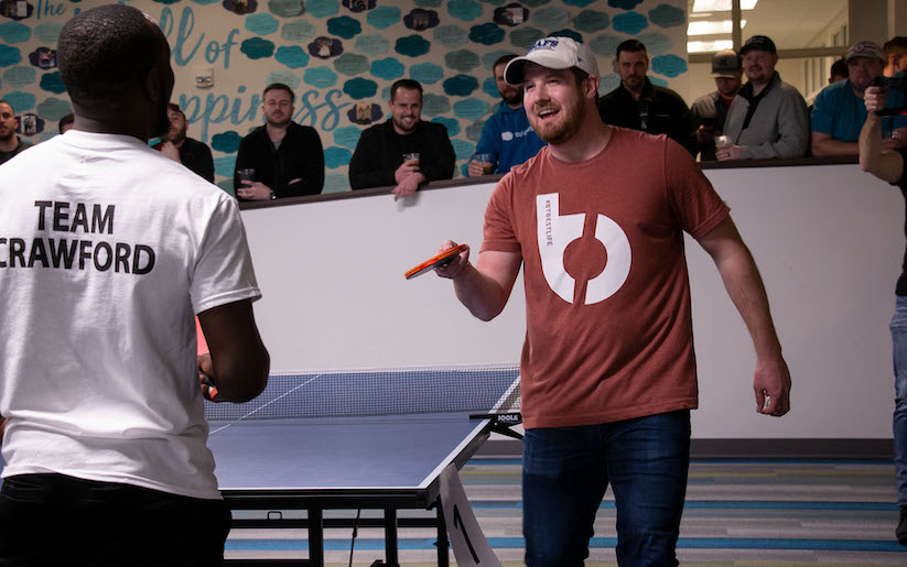 Two players near a ping pong table with people viewing