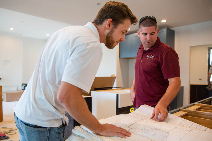 Image of a contractor working with his team member. Both are looking over a blueprint.