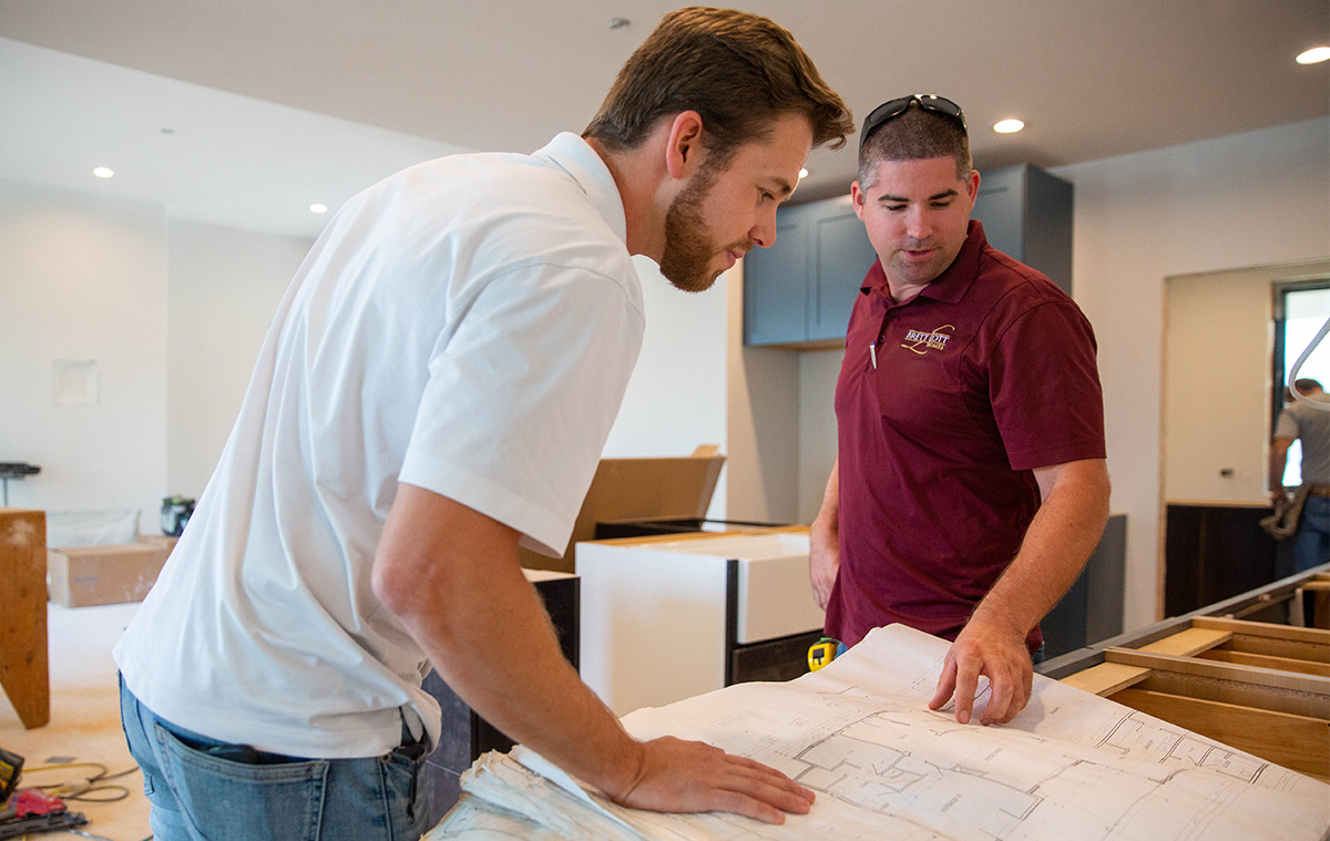 Image of a contractor working with his team member. Both are looking over a blueprint.