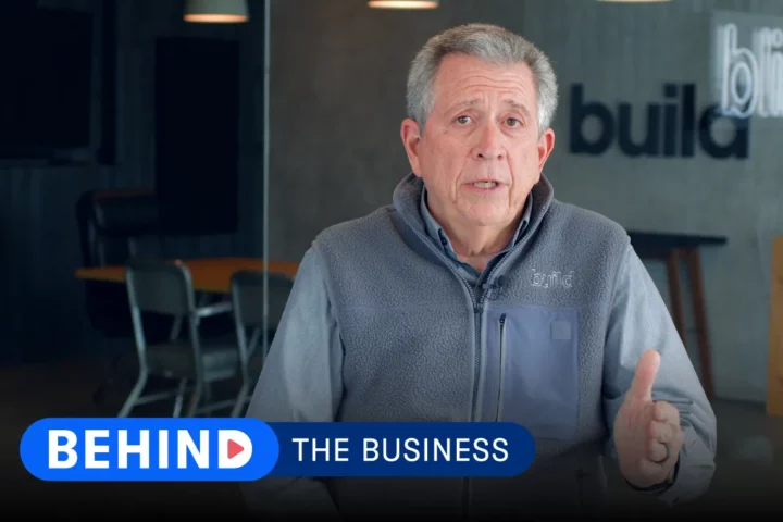 Steve Lesem of Risinger Build talks to camera with a company backdrop behind him and lower-third text in front that reads "Behind the Business."