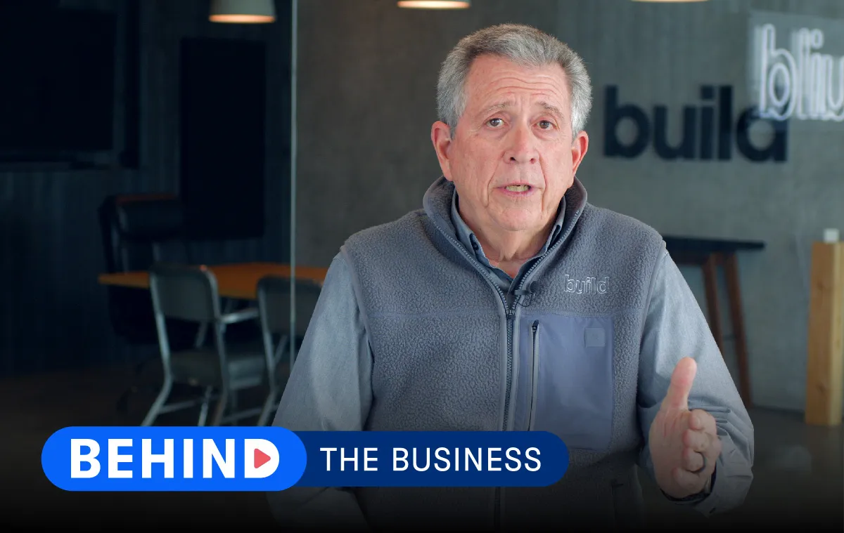 Steve Lesem of Risinger Build talks to camera with a company backdrop behind him and lower-third text in front that reads "Behind the Business."