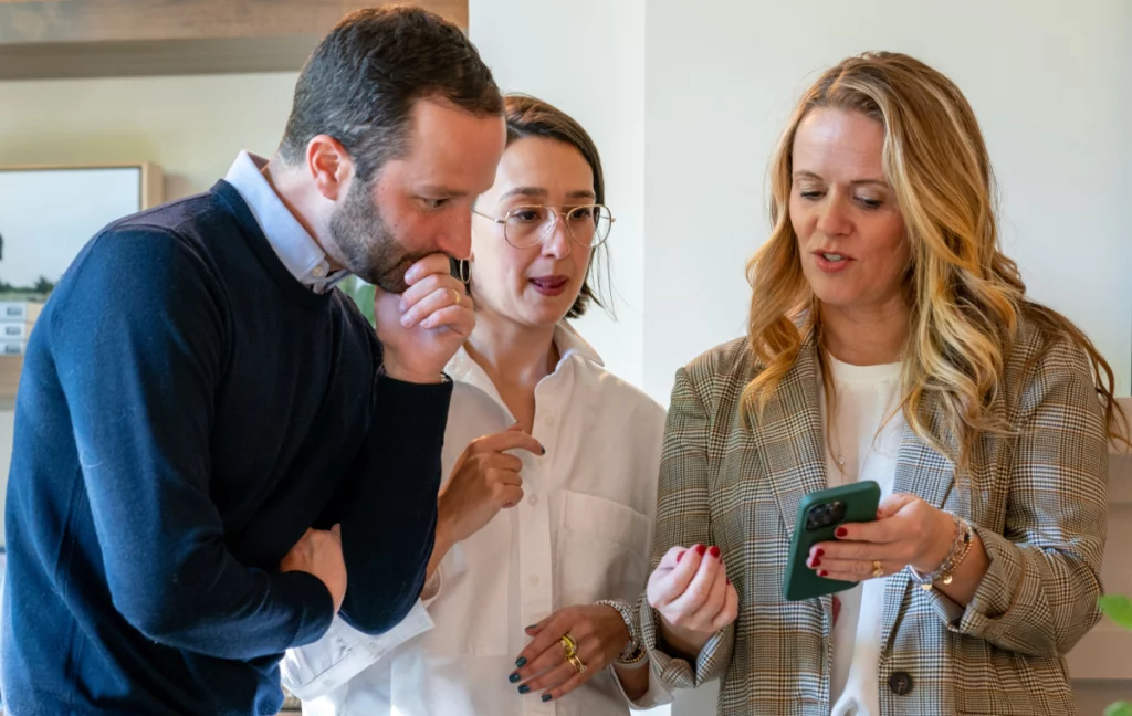 Three people having a discussion, one person is showing their phone to the other people