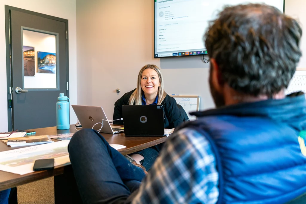 zoomed in over man's shoulder of woman sitting at table behind a laptop and smiling