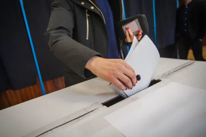 A person putting a voting ballot into a ballot box