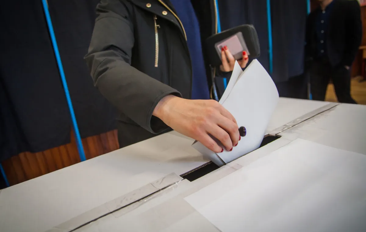 A person putting a voting ballot into a ballot box