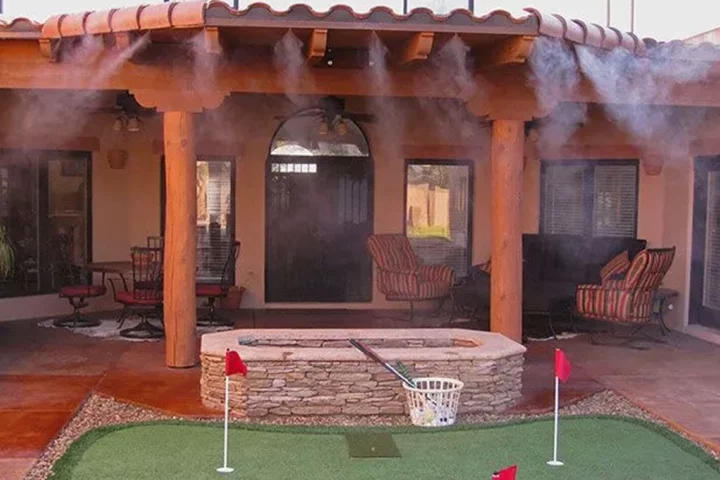A photo of a backyard patio with a fire pit and golf putting area with misters spraying