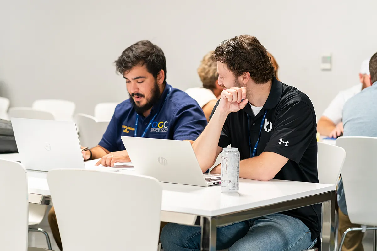 two men sitting at a table in front of their laptops