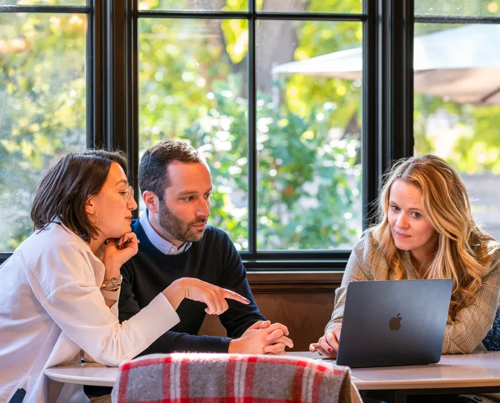 Three people sitting at dining table reviewing laptop