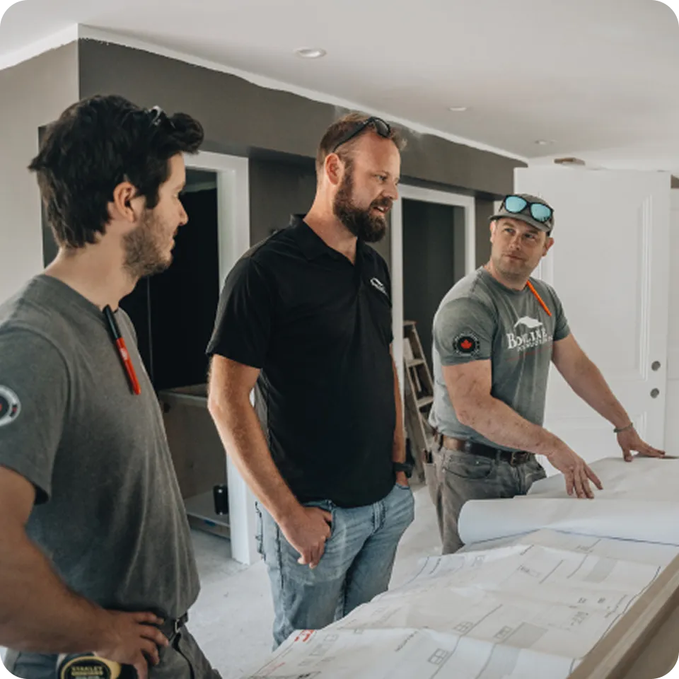 Three construction professionals reviewing blueprints together inside a jobsite