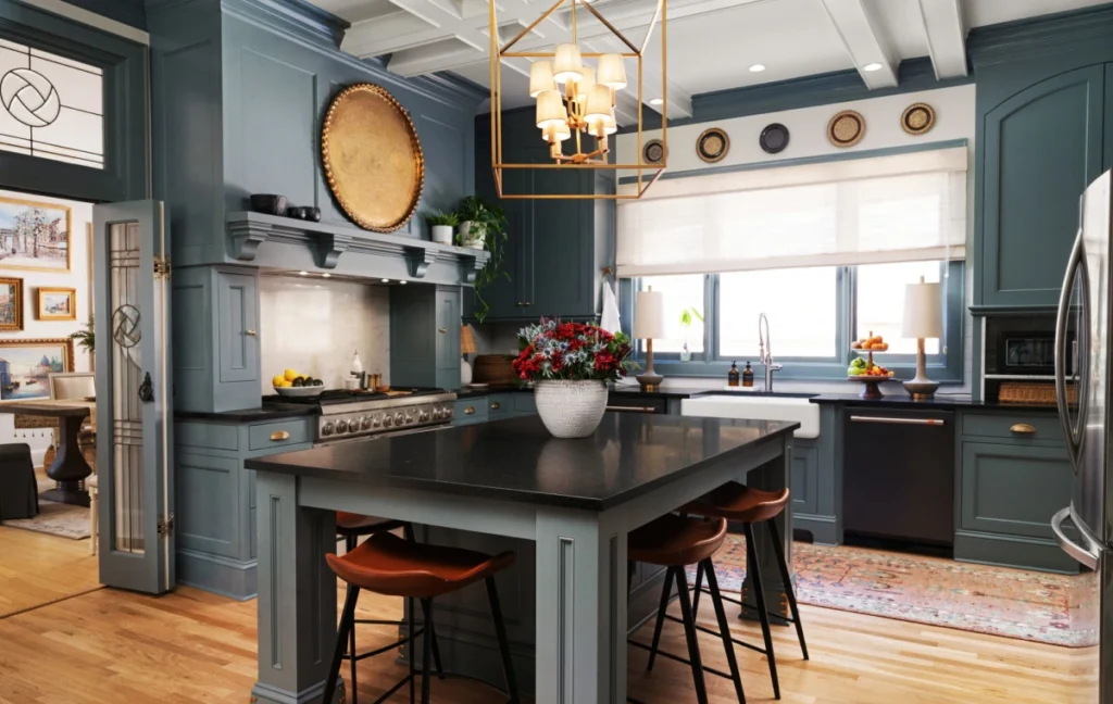 Modern kitchen with blue-gray cabinetry, black island countertop, brass light fixture, and farmhouse sink