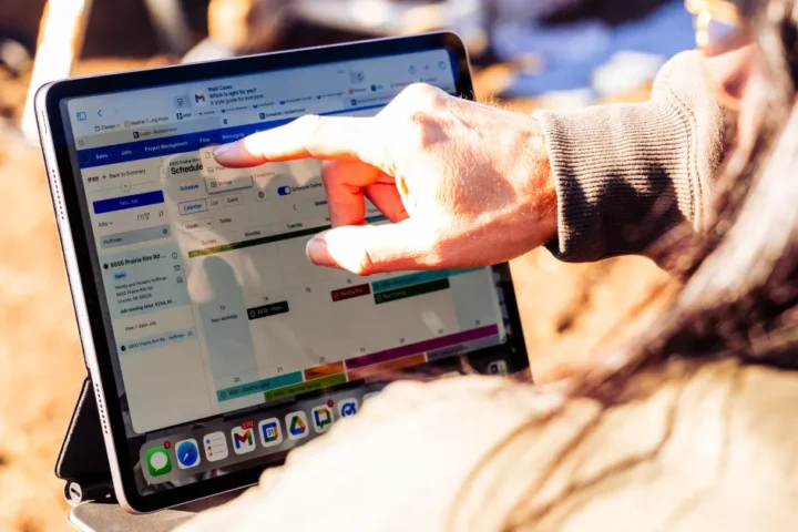 Person using a tablet outdoors to view a Buildertrend construction schedule with tasks and timelines displayed on screen.