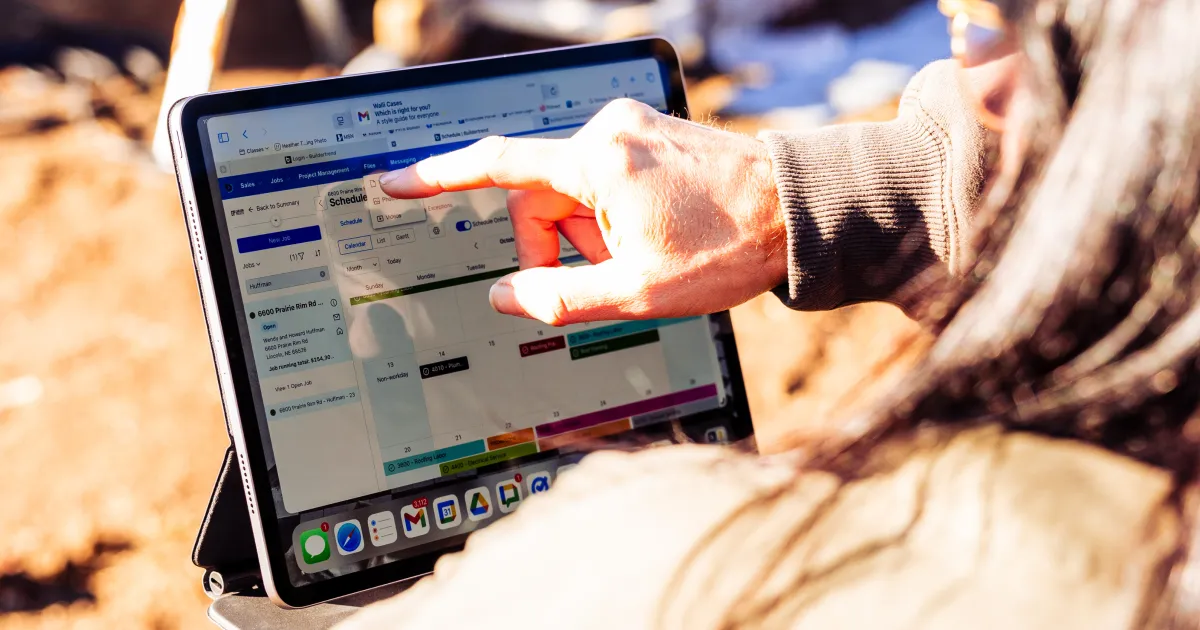 Person using a tablet outdoors to view a Buildertrend construction schedule with tasks and timelines displayed on screen.