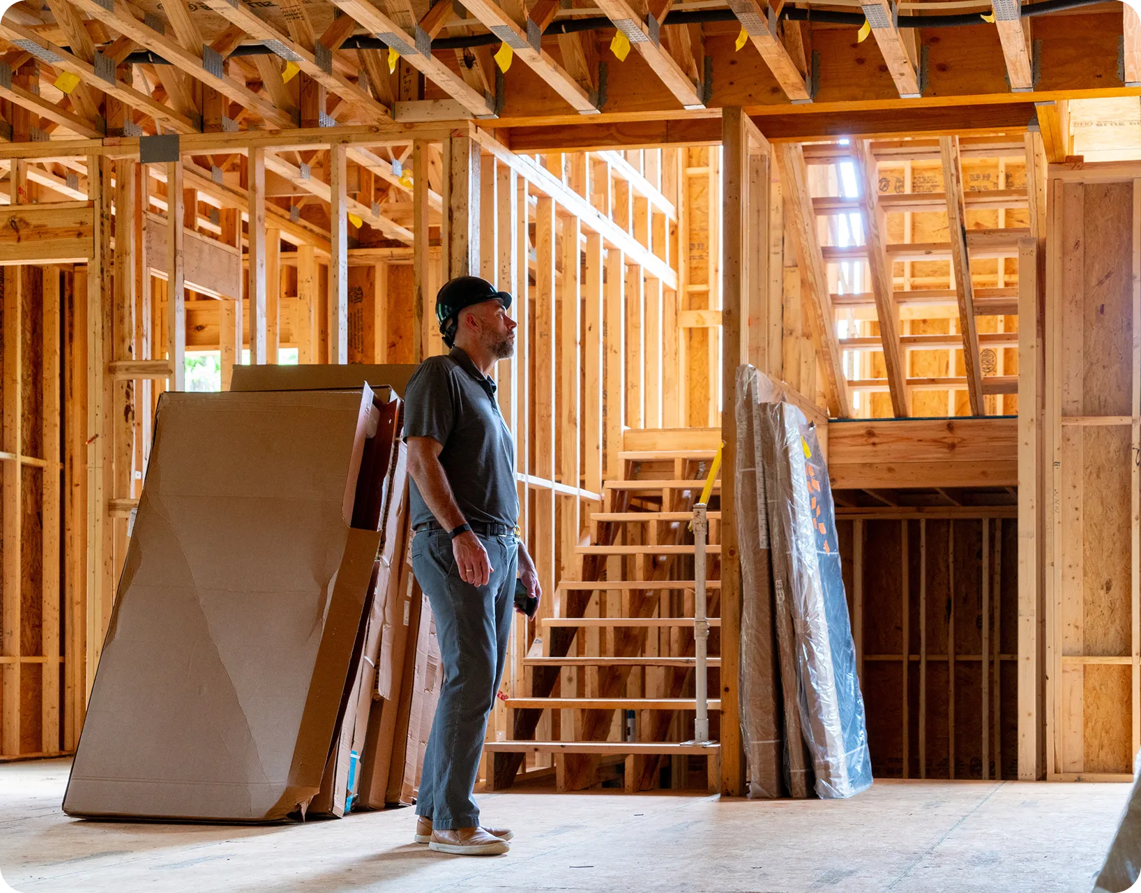 PPC Schedule a Demo 2 A construction worker wearing a hard hat stands inside a partially built house, surrounded by exposed wooden framing, stairs, and building materials.