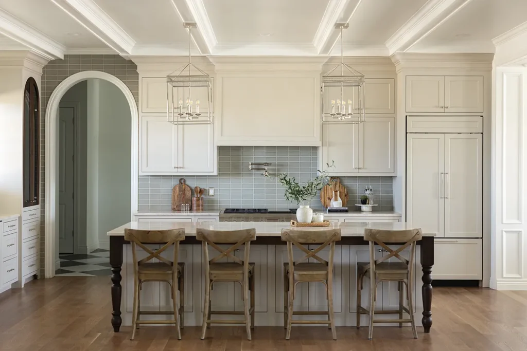 Bright custom kitchen with white cabinetry, large island seating, pendant lighting, recessed ceiling detail, and hardwood floors.