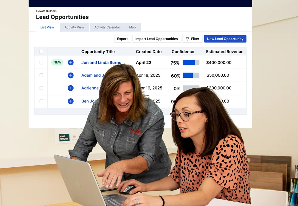 Two coworkers are collaborating at a table while reviewing information on a laptop. One person is actively pointing at the screen, indicating guidance or instruction, while the other types.