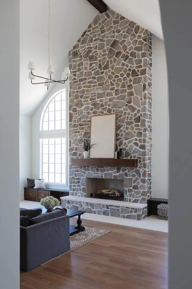 Bright living room featuring a floor‑to‑ceiling stone fireplace, vaulted ceiling, and hardwood floors.