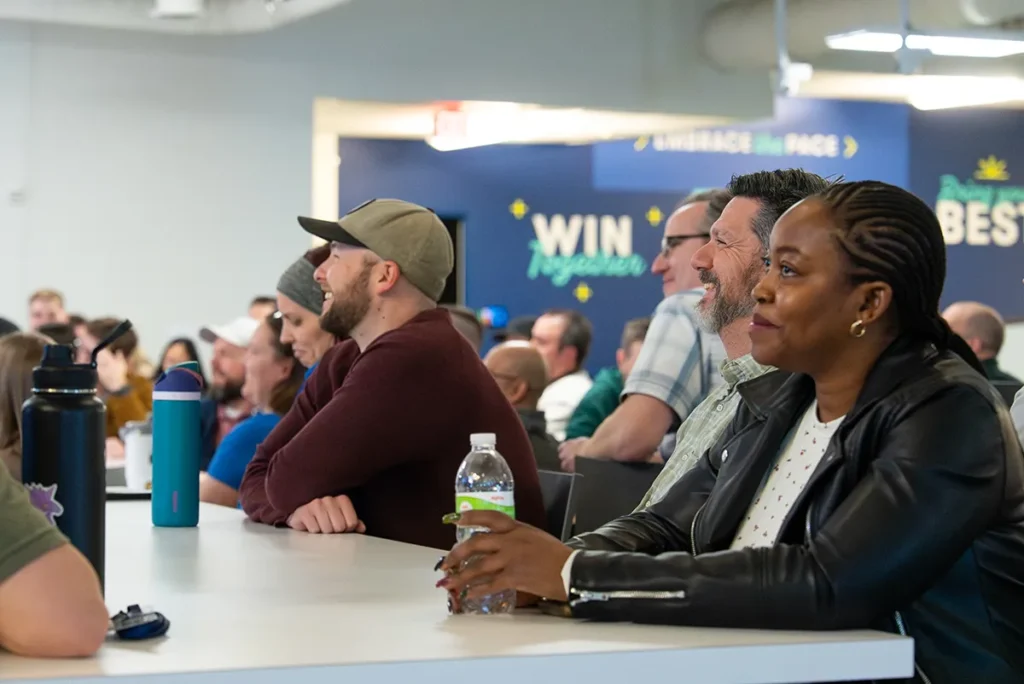 People seated at tables listening to a presentation in the Buildertrend break room.
