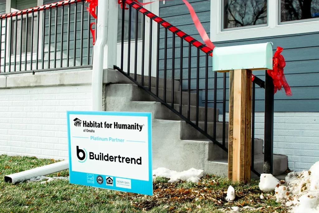 Habitat for Humanity partner home with a Buildertrend sponsorship sign displayed in front of the front porch decorated with red ribbon.