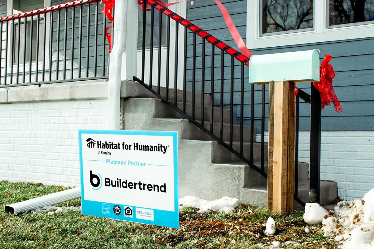 Habitat for Humanity partner home with a Buildertrend sponsorship sign displayed in front of the front porch decorated with red ribbon.