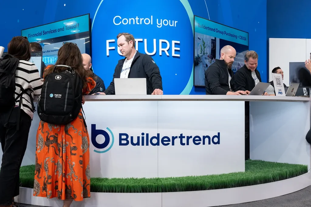 Buildertrend booth at an event with representatives speaking to attendees across a branded counter displaying the company logo and signage that reads ‘Control your future.’”