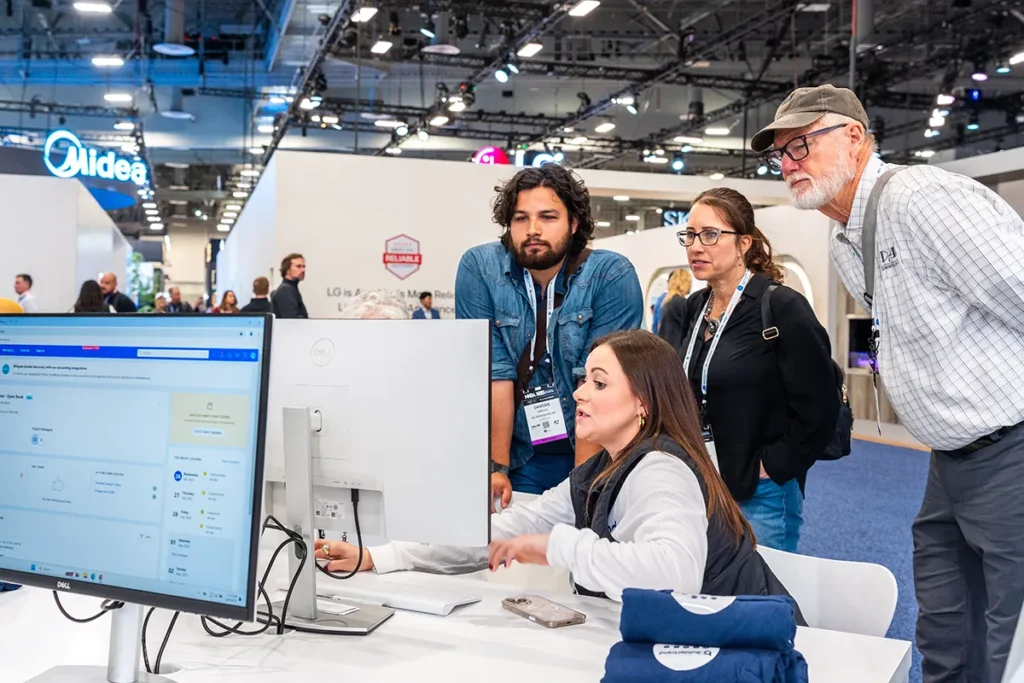 Group gathered around a computer workstation at a trade show booth watching a software demonstration.