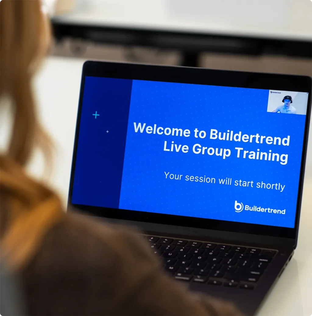 Person viewing laptop screen displaying "Welcome to Buildertrend Live Group Training" welcome message with instructor visible in video call window in upper right corner