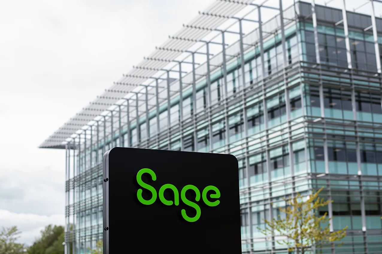 Sage Intacct 2 Sage company sign with green logo displayed on black background in front of modern glass and steel office building
