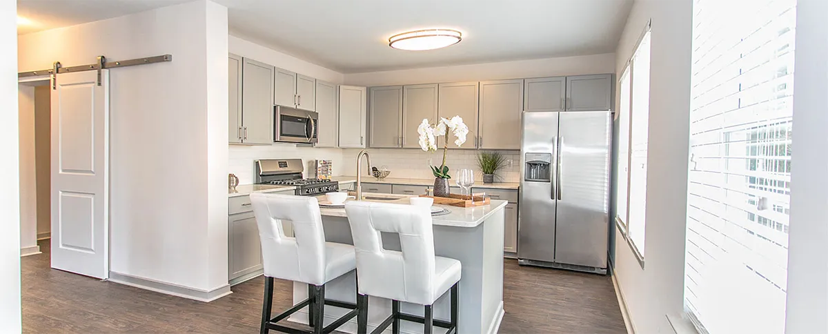A clean NOVUS custom kitchen has white chairs, sliding doors, and a crisp white countertop.