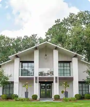 Top 5 construction project management best practices 2 Modern two-story white house with symmetrical design, featuring a central entrance with black double doors, large windows, columned portico, and manicured landscaping with topiary plants and trees in background.