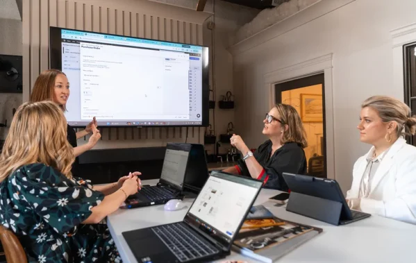A group of women in a meeting room looking at Buildertrend product screen on a large monitor