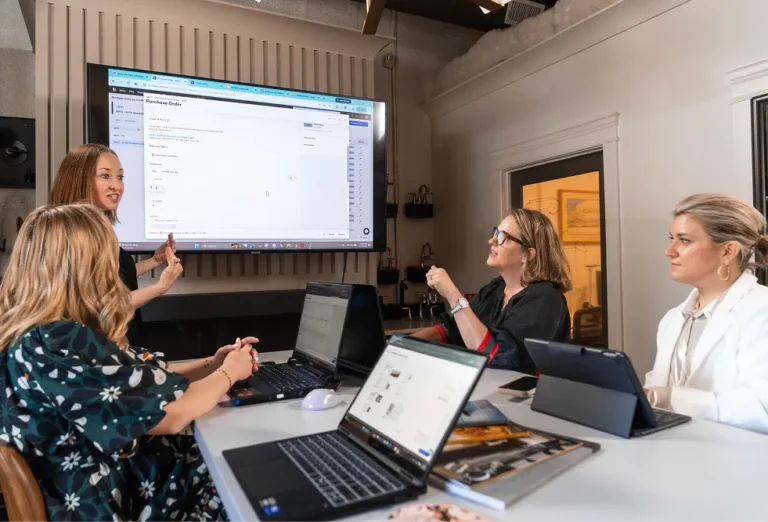 A group of women in a meeting room looking at Buildertrend product screen on a large monitor
