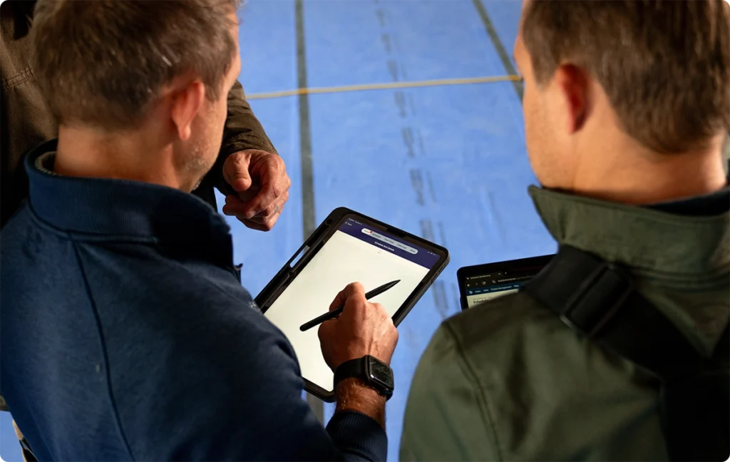 Construction professionals reviewing project information on tablets during a jobsite meeting.