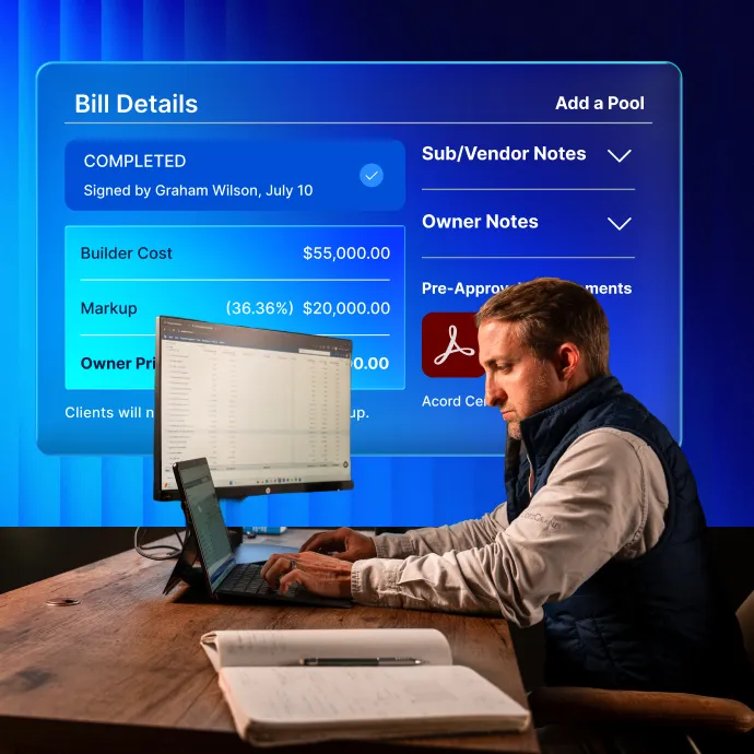 Construction AI Software 1 A man in business casual attire sits at a wooden desk, viewing a laptop while looking at a large blue-tinted display screen showing bill details including builder costs, markup percentages, and various notes sections. Documents are visible on the desk in front of him.