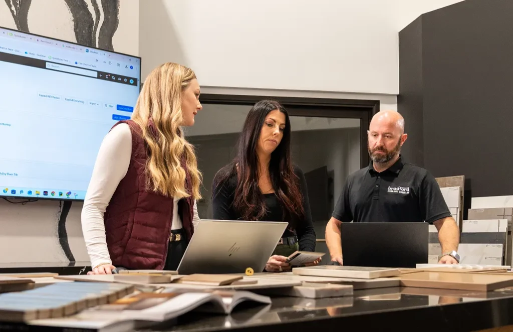 Three construction professionals reviewing project estimates on laptops in a design showroom.