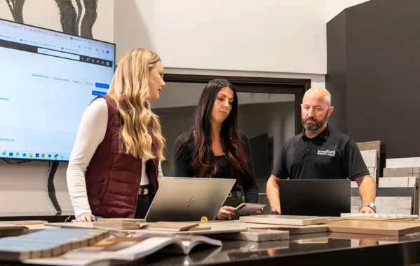 Three construction professionals reviewing project estimates on laptops in a design showroom.
